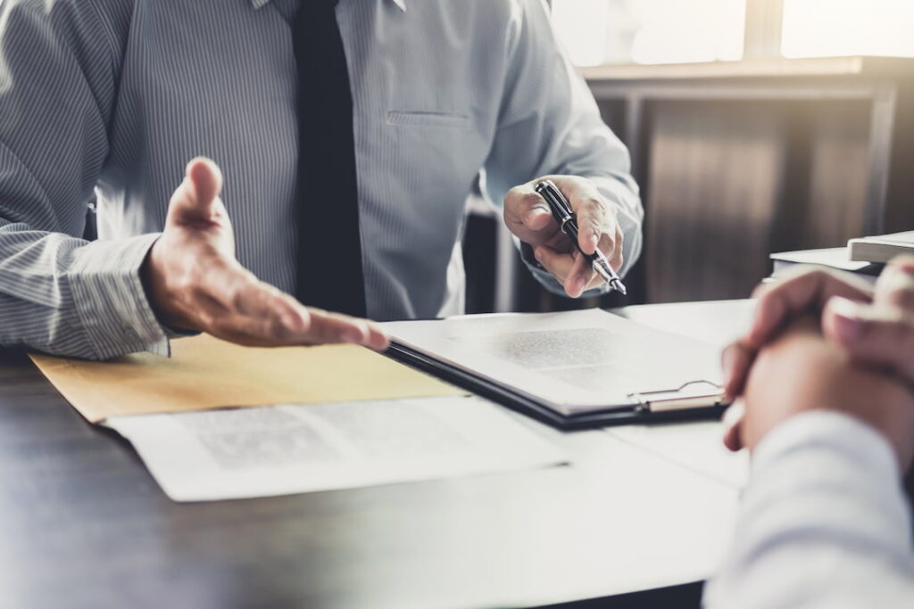 two people sit at a desk with a document prepared to sign between them