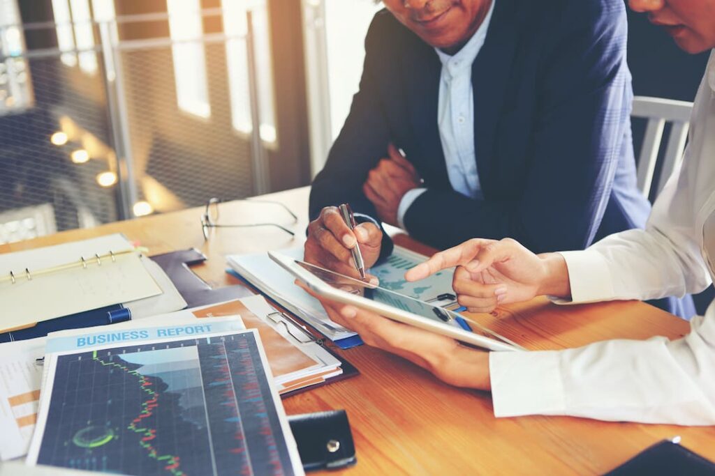 two people point at tablet screen while meeting with business plans
