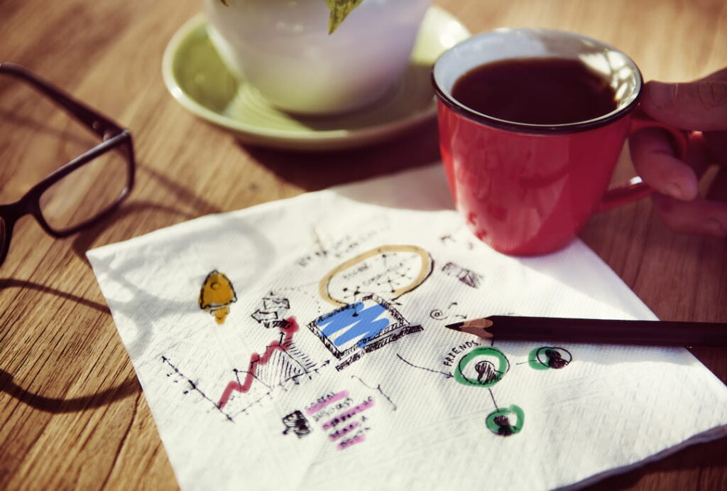 a cup of coffee set down on top of a napkin that holds business idea scribbles