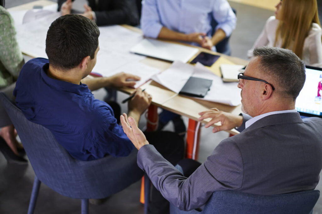 a business meeting with boss and employees sitting around a conference table with scattered documents