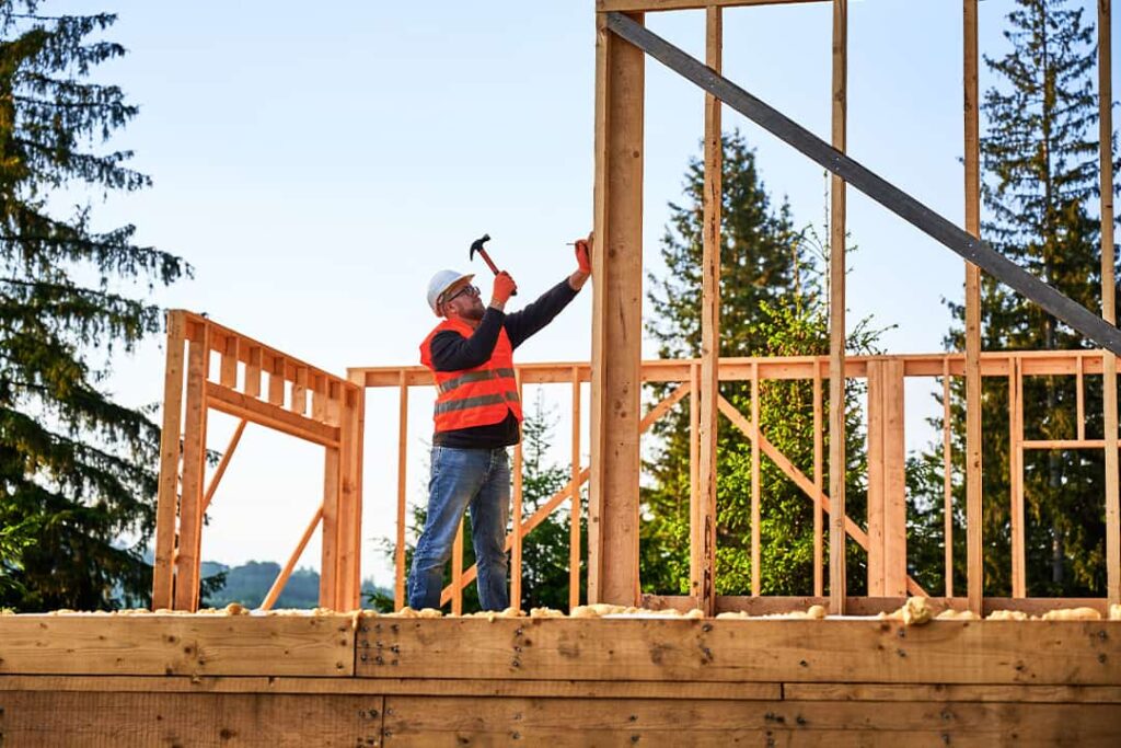 contruction worker hammers nails into house wooden framing