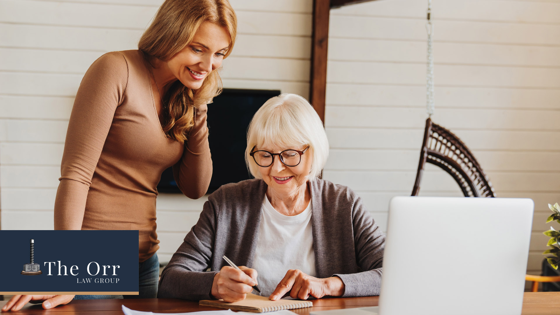 Mother sitting at desk signing paper to establish power of attorney with supportive daughter standing beside her